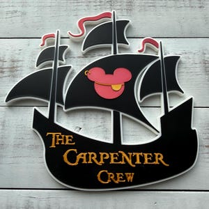 May include: A black and white ship-shaped wall decoration with red accents. The ship's sails feature a pink Mickey Mouse head with a gold earring. The text "The Carpenter Crew" is in gold lettering.