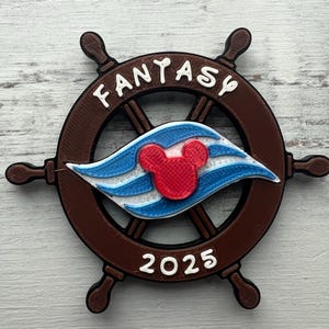 May include: A brown wooden ship's wheel with a white Mickey Mouse head and the word "Fantasy" written around the rim. The wheel has a blue and white striped sail with a red Mickey Mouse head in the center. The year 2025 is written at the bottom of the wheel.