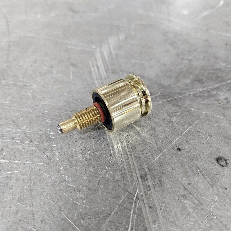 May include: A gold-colored metal valve with a threaded stem and a ball-shaped tip. The valve has a black rubber seal and a ribbed design.