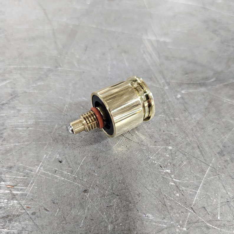May include: A gold-colored metal valve with a black rubber seal and a silver ball at the end of the stem.