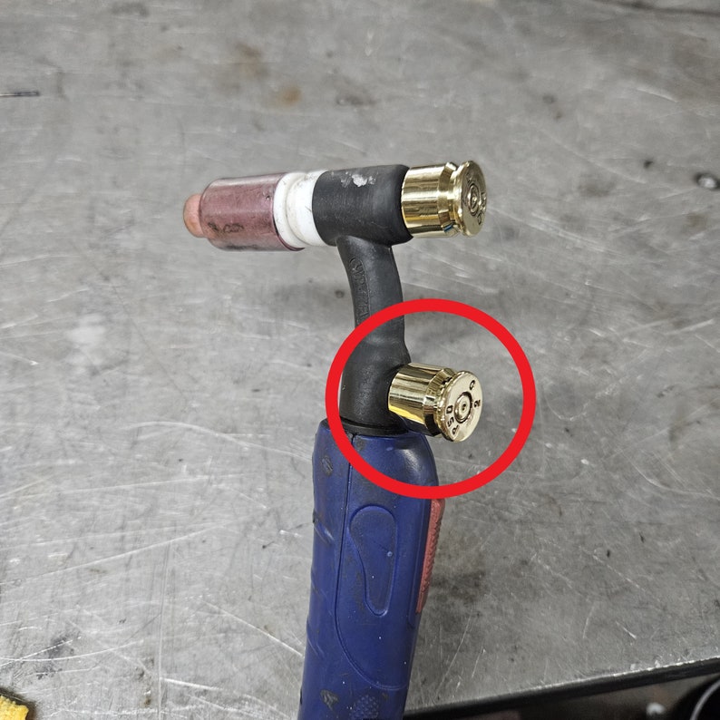 May include: A close-up of a welding torch with two gold-colored caps. The caps are made from spent bullet casings.