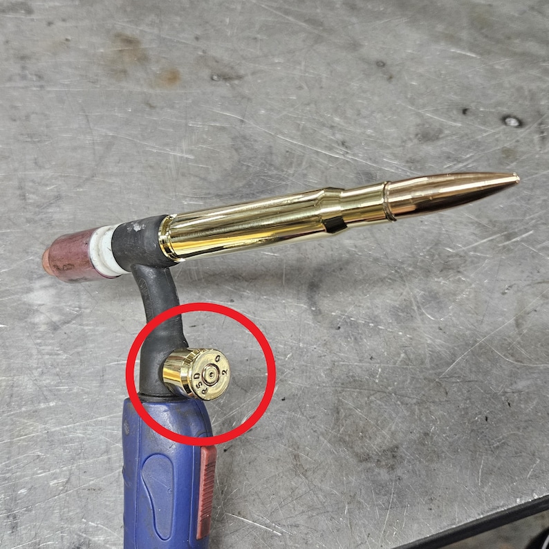 May include: A gold-colored welding torch with a blue handle. The torch is made from a repurposed .50 caliber bullet casing. The bullet casing is visible on the torch's handle.