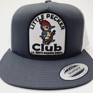 May include: A gray and white trucker hat with a patch featuring a cartoon woodpecker and the text "Little Pecker Club Lil Gents Making Dents". The hat has a white mesh back and a gray brim.