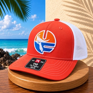 May include: An orange and white trucker hat featuring a circular patch with a white alligator silhouette over a blue and orange background. The front panel displays a black sticker with the text 112 The Original MD-LG and a red R logo.