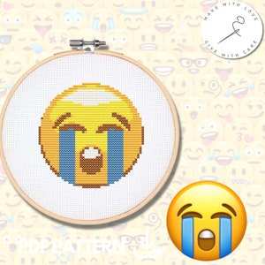 Puede incluir: Patrón de punto de cruz de un emoji amarillo llorando con lágrimas azules. El patrón se muestra en un aro de bordado de madera.
