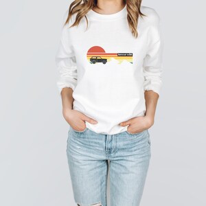 May include: White sweatshirt with a retro sunset graphic, a black silhouette of a jeep, and the text "forever wild".