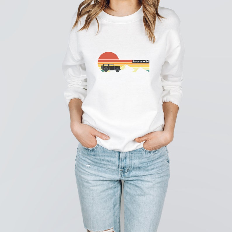 May include: White sweatshirt with a retro sunset graphic, a black silhouette of a jeep, and the text "forever wild".