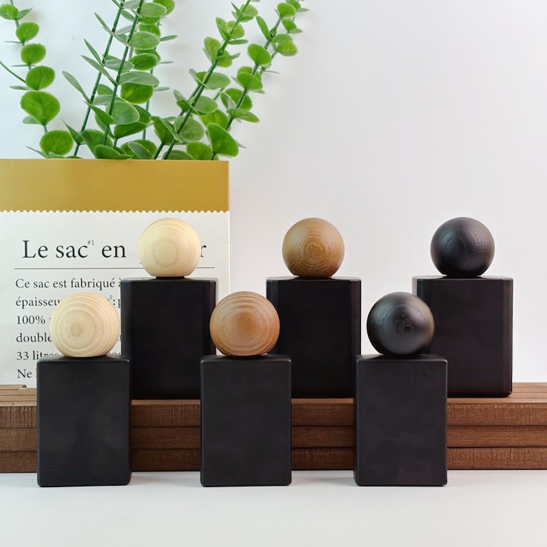 May include: Six decorative wooden objects. Each object has a black rectangular base topped with a wooden sphere. The spheres vary in color, including light and dark wood tones. The objects are arranged on a wooden surface.