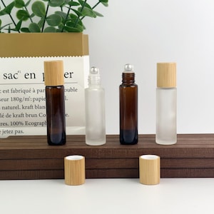 May include: Four glass roll-on bottles with bamboo lids. Two bottles are amber, and two are frosted. The bottles are displayed on a dark brown wooden surface. The image also includes two separate bamboo lids.