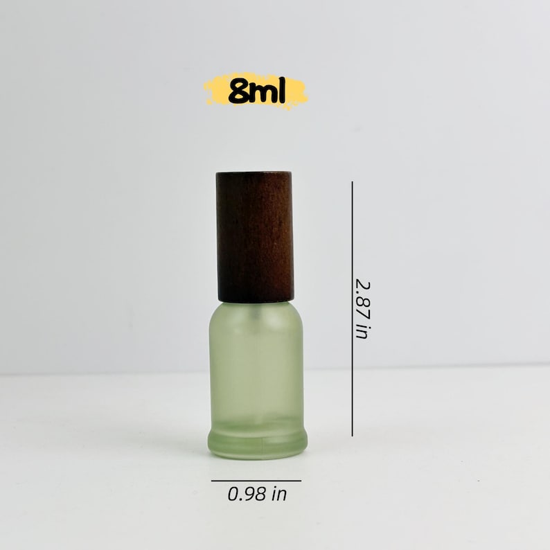 May include: A small, frosted glass bottle with a dark brown wooden cap. The bottle is 7.3 cm tall and 2.5 cm wide. The text "8ml" is displayed above the bottle.
