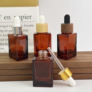 May include: Four amber glass dropper bottles with different cap styles. One has a silver cap with a white dropper, another has a bamboo cap, and a third has a dark wood cap. A fourth bottle is uncapped, with a dropper nearby.