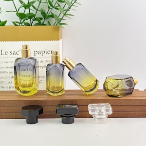 May include: Several perfume bottles with gold sprayers and a gradient color scheme of yellow and blue. The bottles are rectangular with rounded edges. Three black and one clear bottle stoppers are in the foreground. The background includes a paper bag with text.