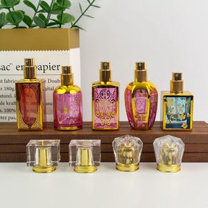 May include: An assortment of decorative perfume bottles with gold-colored tops and ornate designs. The bottles are various shapes and sizes, with pink, blue, and clear glass. The bottles are displayed on a wooden surface.