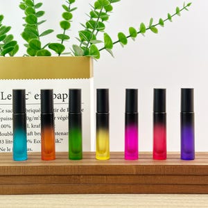 May include: Seven cylindrical glass roller bottles with black caps, each featuring a unique gradient color transition from black at the top to a vibrant hue at the base, including blue, orange, green, yellow, pink, red, and purple.