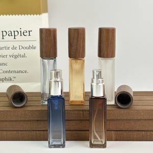 May include: A collection of rectangular glass perfume bottles with wooden caps. The bottles are clear, amber, and brown, with silver spray nozzles. One bottle is blue. The caps are cylindrical.