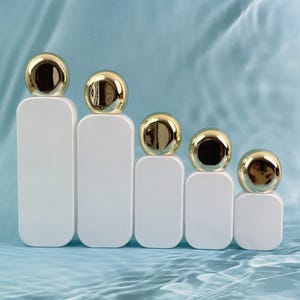 以下が含まれることがあります： 丸みを帯びた角を持つ5つの白い長方形のボトル。それぞれが光沢のある金色の球で覆われています。ボトルは左から右へサイズが小さくなり、視覚的な階段効果を生み出しています。背景は水のような模様の淡い青色です。