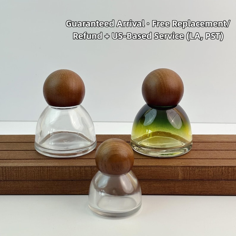 May include: Three glass bottles with wooden stoppers. One bottle is clear, another has a green and yellow gradient, and the third is also clear. The bottles are arranged on a brown wooden surface.