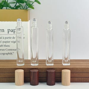 May include: Four clear glass roll-on bottles with silver rollerballs and wooden caps. Two caps are light wood, and two are dark wood. The bottles are rectangular and sit on a wooden surface.
