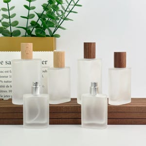May include: Several frosted glass perfume bottles with wooden and silver-coloured caps. The bottles are rectangular and arranged on a wooden surface. Some bottles have light-coloured wooden caps, others have darker brown caps.