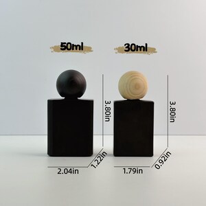 May include: Two black rectangular perfume bottles with wooden spherical tops. The bottles are 3.80 inches tall. One bottle has a dark top, the other a light wood top. The bottles are labeled 50ml and 30ml.