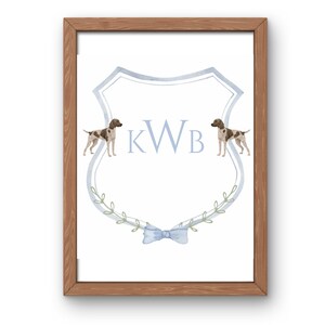 May include: A light blue and white watercolor monogram with the initials "KWB" surrounded by a wreath of green leaves and two brown and white dogs. The monogram is on a light blue shield with a light blue bow at the bottom.