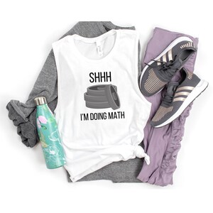 May include: White sleeveless tank top with the text "SHHHH I'M DOING MATH" and a graphic of a stack of weight plates.