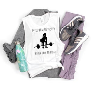 May include: White sleeveless shirt with the text "Every woman should know how to clean" and a silhouette of a woman lifting a barbell.