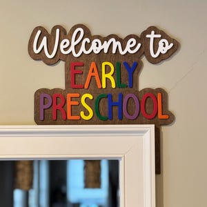 May include: Welcome to Early Preschool sign with rainbow colored letters on a brown wooden background.