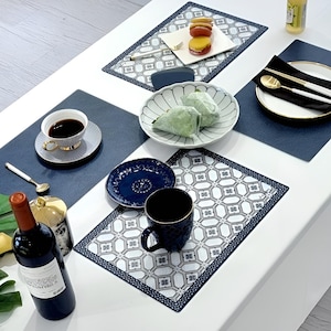 May include: A dining table set with a variety of items. Features a wine bottle, coffee cup, plates with food, and patterned placemats. The colour scheme is mainly white, navy blue, and gold, creating an elegant aesthetic.