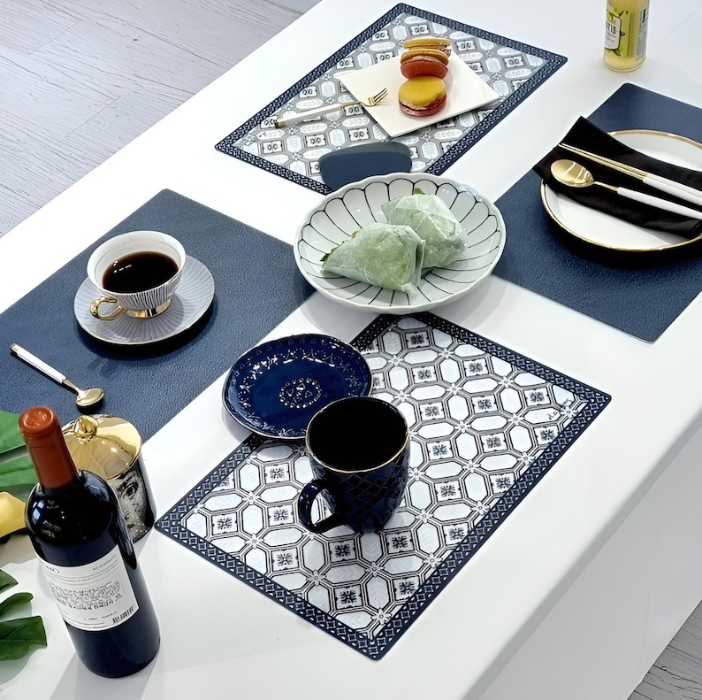 May include: A dining table setting with various items. Includes a bottle of wine, a cup of coffee, plates with food, and patterned placemats. The color scheme is primarily white, navy blue, and gold, creating an elegant aesthetic.
