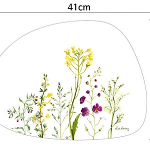 May include: A placemat with a white background and a watercolor floral design. The placemat is 16 inches wide and 12 inches tall. The floral design features yellow, purple, and white flowers and green foliage.