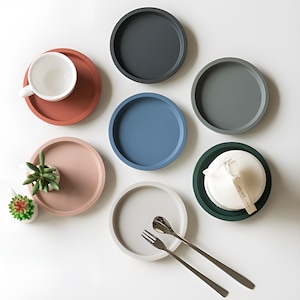 May include: Set of six round silicone coasters in various colors, including gray, blue, pink, and green. The coasters are arranged on a white surface.
