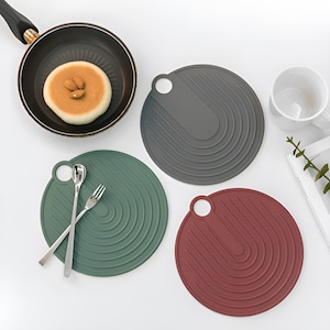 May include: Three round silicone pot holders in grey, green, and red. Each pot holder has a circular handle and a concentric circle design.