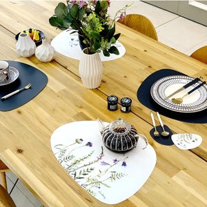 May include: A wooden dining table set with various decorative items. Includes white vases, a teapot, plates, and placemats. The placemats have floral designs. The table is set for a meal with silverware and small jars.