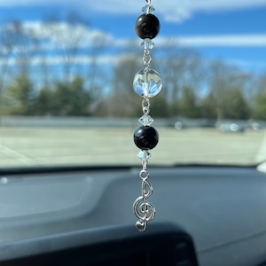 May include: A silver car charm with a treble clef and black and clear glass beads hanging from a silver chain.