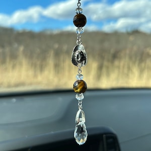 May include: A silver car charm with a horseshoe pendant, tiger's eye beads, and crystal accents. The charm hangs from a silver chain.