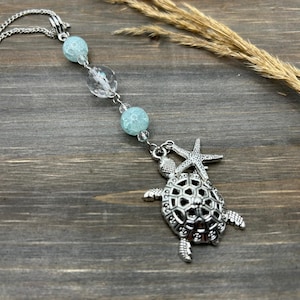 May include: A silver charm necklace with a turtle and starfish design. The necklace features clear and light blue beads.