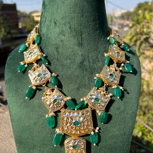 May include: A gold and green statement necklace with multiple tiers of emerald green beads and gold pendants. The pendants are decorated with intricate designs and white stones.