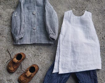 Puede incluir: Un conjunto de ropa de muñeca en miniatura que incluye una camisa gris abotonada, una camiseta sin mangas blanca y pantalones vaqueros azules con puños doblados. Zapatos de cuero marrón con cordones completan el conjunto. La ropa está sobre una superficie gris.