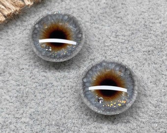 May include: Two gray and brown glass eyes with glitter and a white stripe. The eyes are round and have a realistic look.