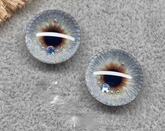May include: Two gray and brown glass eyes with white stripes and silver glitter. The eyes have blue and silver accents.