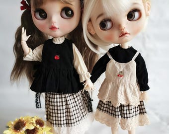 Puede incluir: Dos muñecas de moda con ojos grandes y rasgos detallados. Una muñeca tiene cabello castaño y un lazo rojo, la otra tiene cabello rubio. Ambas muñecas visten faldas a cuadros en blanco y negro, tops negros y zapatos negros. Un ramo de girasoles está cerca.