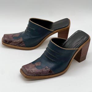 May include: A pair of dark teal leather mules with a square toe and a snakeskin pattern on the vamp. The shoes have a wooden block heel and a leather insole. The mules are open-backed and have a slip-on design.