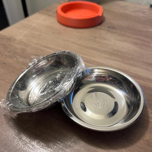May include: Two stainless steel pet bowls, one stacked on top of the other. The top bowl is wrapped in plastic.