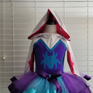 Peut inclure: Costume à capuche blanc avec un motif d'araignée violet et bleu sur le corsage et une jupe en tulle à plusieurs épaisseurs avec des bordures de ruban violet et bleu.