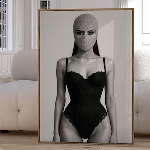 Puede incluir: Impresión en blanco y negro enmarcada que presenta a una persona con un pasamontañas gris y un body negro con adornos de encaje. La obra de arte se exhibe en una habitación luminosa con paredes blancas y suelo de madera.