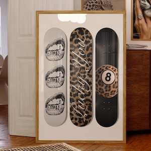 May include: A framed artwork featuring three skateboard decks. One deck has a leopard print with the words "Lucky You." Another deck has a black background with a leopard print 8-ball. The third deck has a gray background with three sets of lips.