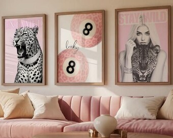 May include: Three framed wall art pieces with a pink and neutral color palette. One features a roaring leopard with the word "UNTAMED". Another shows two pink billiard balls with the number 8 and the word "lucky". The third has a woman with a leopard and the words "STAY WILD".