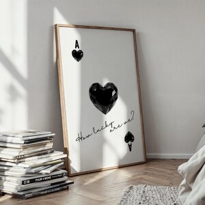 May include: A framed print with a black and white illustration of an ace of spades playing card. The ace of spades is depicted as a black heart with the letter A at the top. The text "How lucky are we?" is written in cursive below the heart.