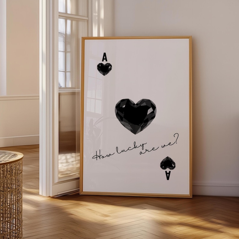 May include: A white poster with a black ace of hearts playing card design. The heart is a large, geometric shape. The text "How lucky are we?" is written in black cursive script.